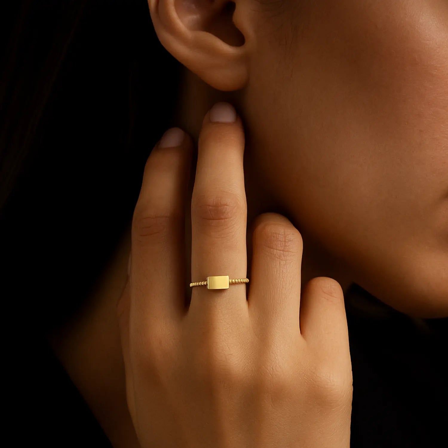 Detail ruky ženy so zlatým minimalistickým prsteňom na prste, jemný šperk na tmavom pozadí