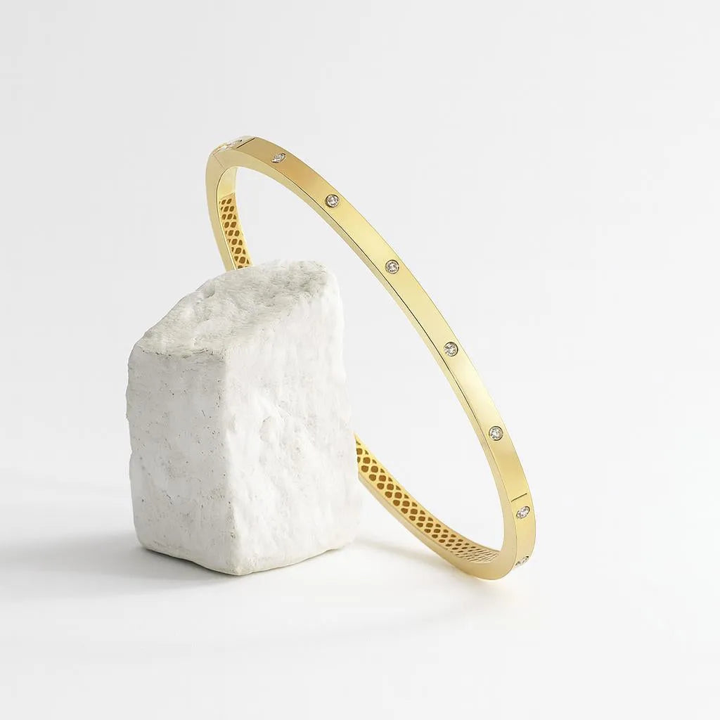 Zlatý náramok CREYO STRUCTURA opretý o biely kameň – umelecký detail