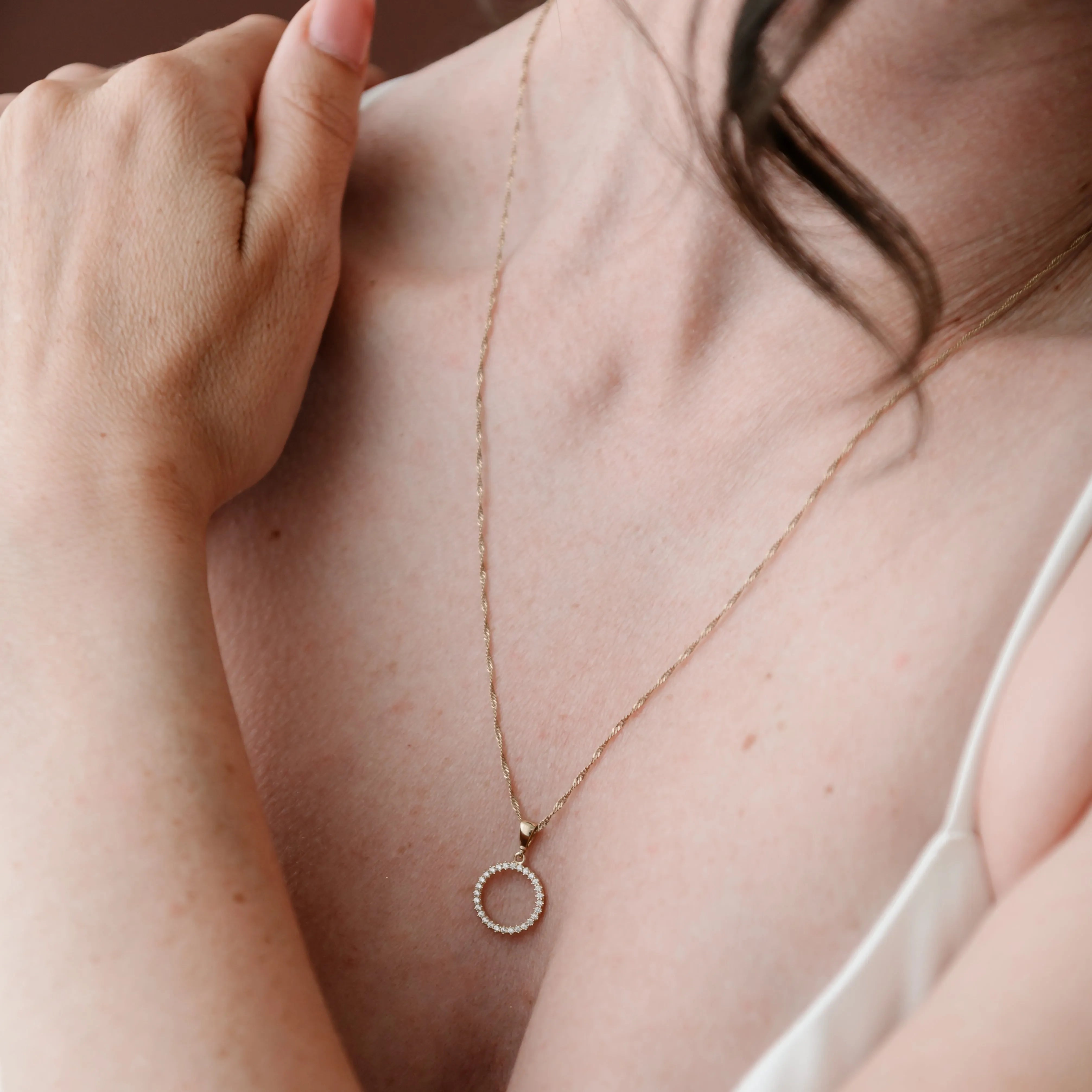 Zlatý prívesok s čírymi zirkónmi v tvare kruhu na krku ženy v bielej blúzke – kolekcia CREYO LINEA