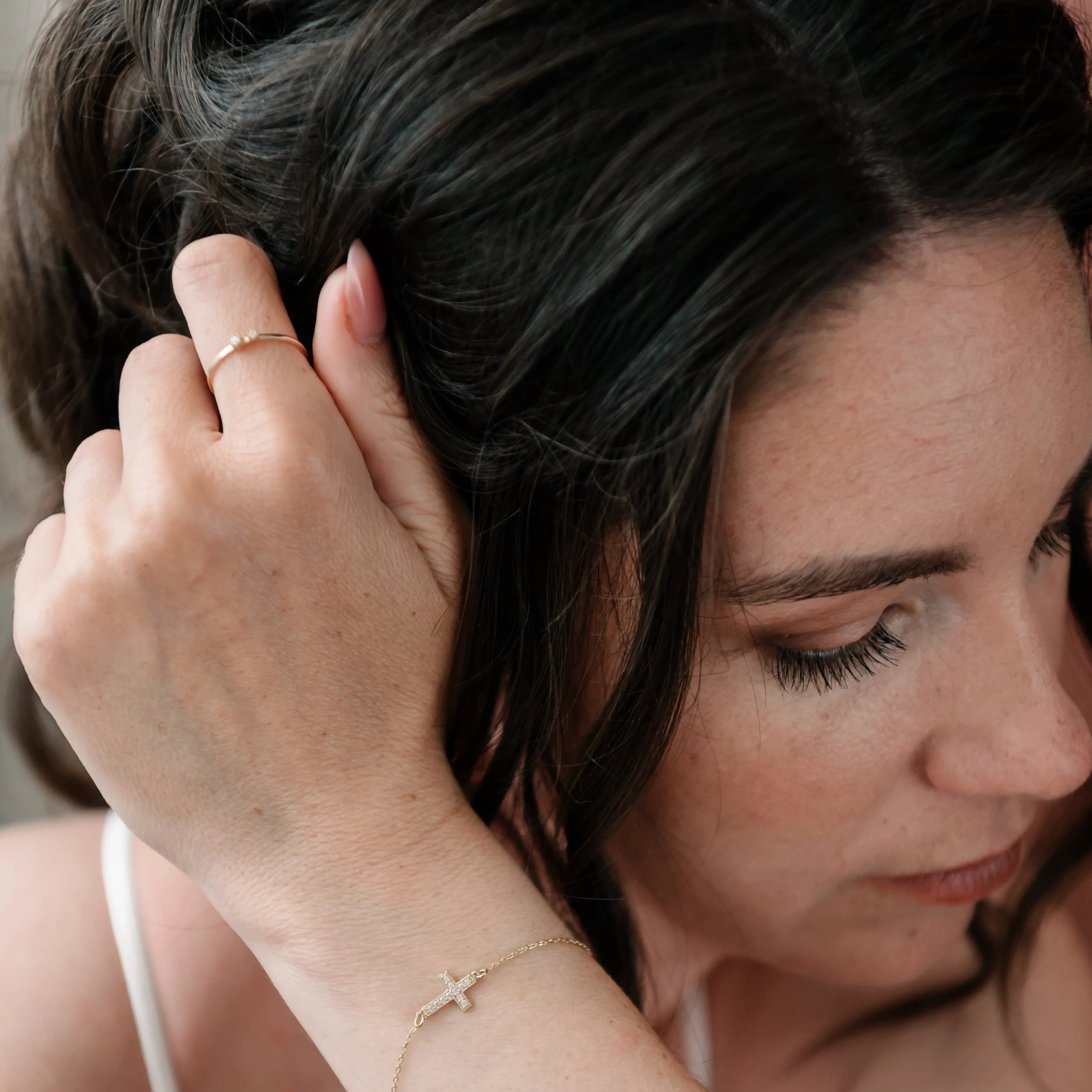 Žena nosí jemný zlatý náramok CREYO s krížikom a zirkónmi